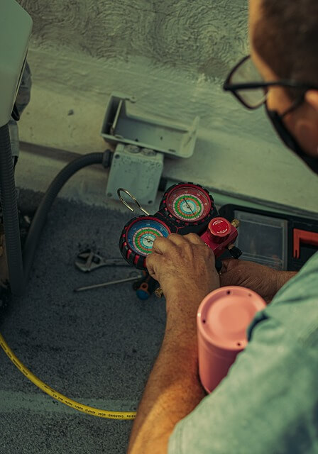 Technician using HVAC manifold gauges to measure and adjust system pressure during maintenance.