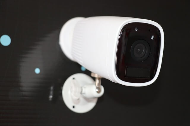 A white security camera mounted on a wall, positioned for surveillance.