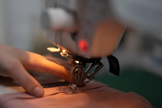 Close-up of a sewing machine stitching fabric with a person’s hand guiding the material.