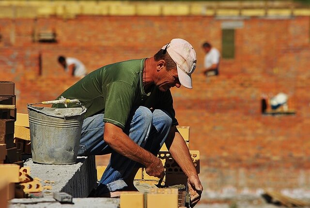 Mason working on a brick wall construction site with a bucket and masonry tools